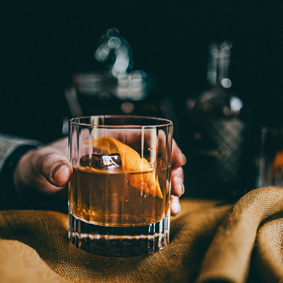 Close-up of a hand holding a glass of Negroni cocktail with an orange peel garnish.