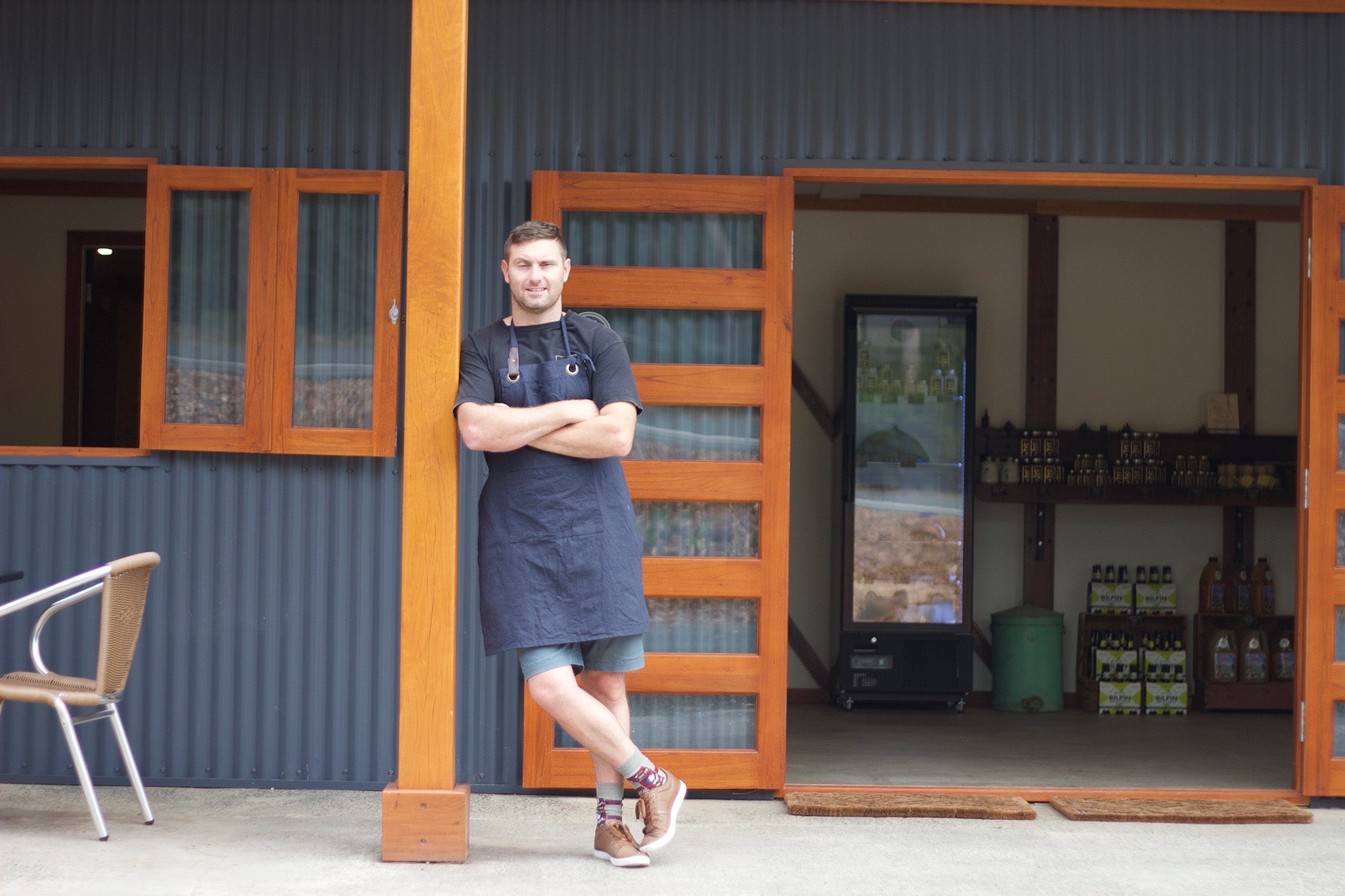 Man in an apron standing outside a store in Bilpin, showcasing local bush honey and products.