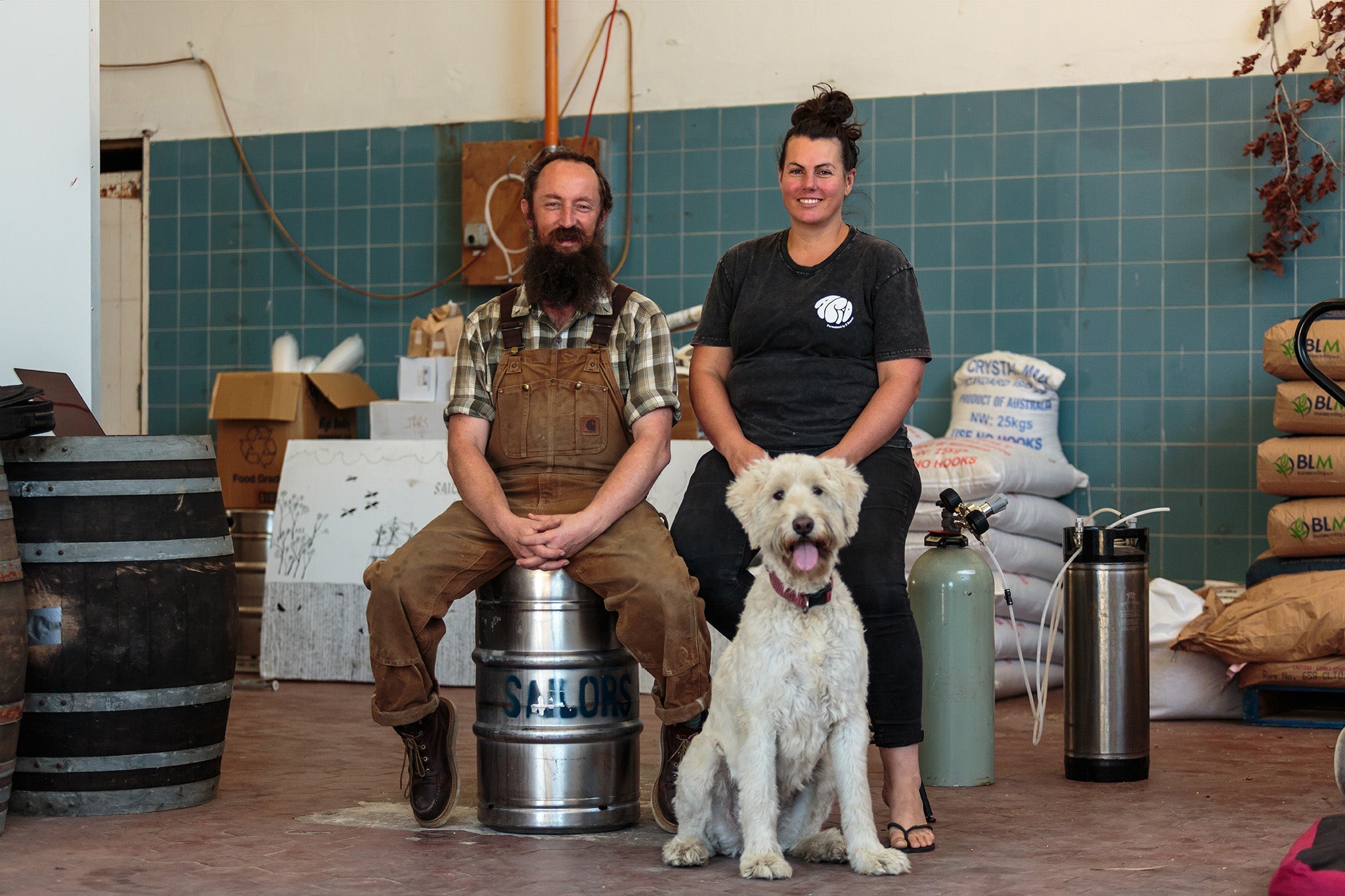 Sailors Grove couple in brewery with dog, showcasing craft beer passion and innovation in a rustic setting.