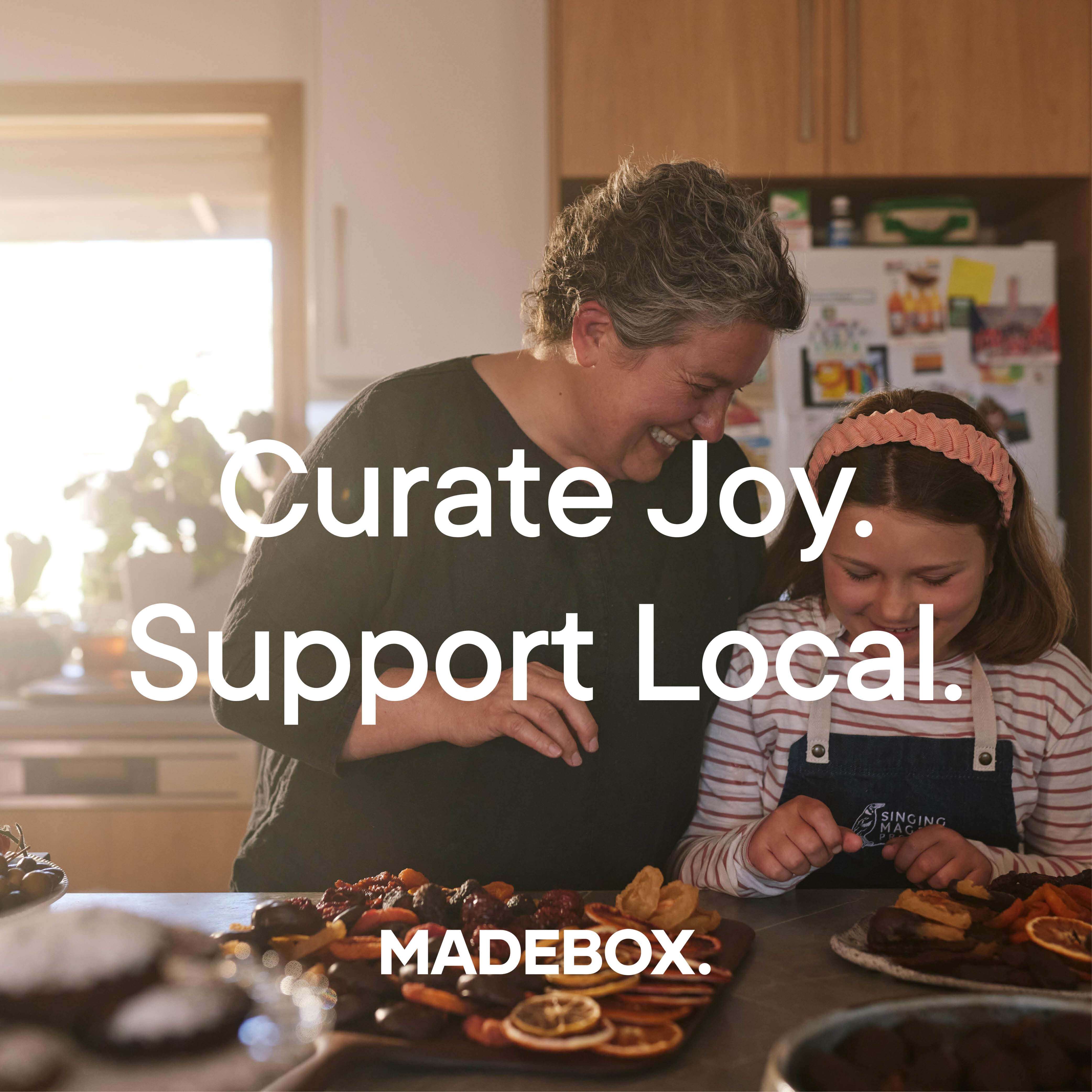 Two women happily preparing festive treats in a cozy kitchen, celebrating local joy and food.
