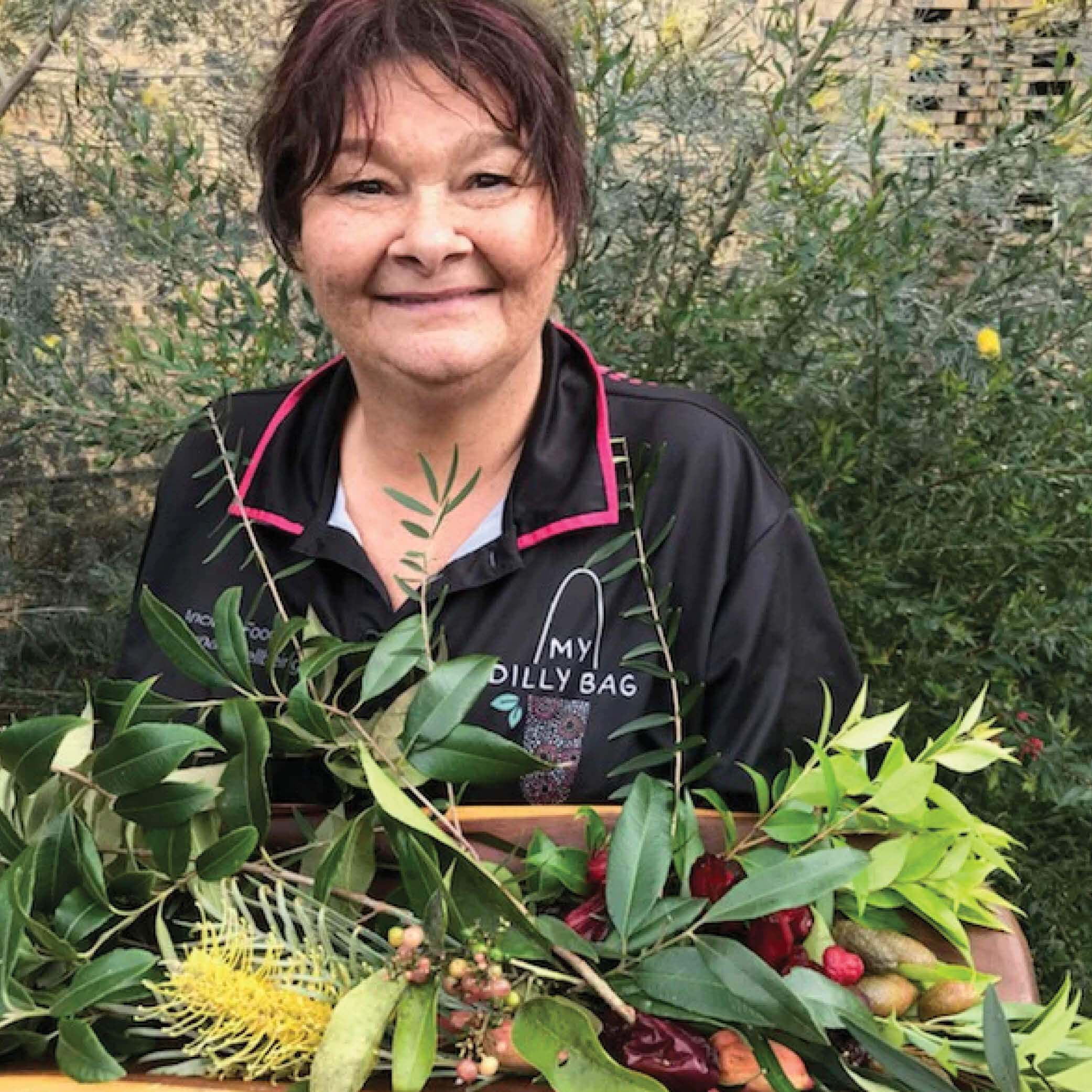 Smiling woman holding a tray of native Australian plants and fruits, showcasing local flora.