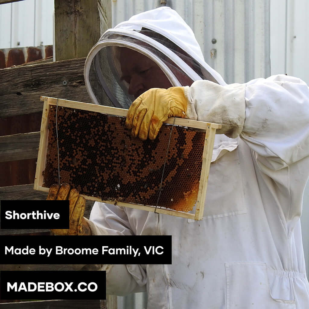 Beekeeper inspecting honeycomb frame, showcasing artisanal honey from Broome Family, VIC.