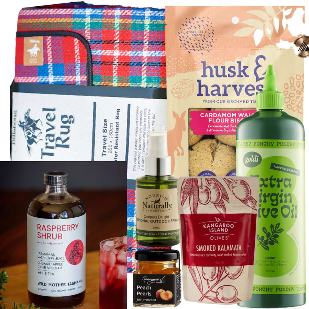 The Picnic Box featuring a travel rug, raspberry shrub, olives, and gourmet snacks for outdoor enjoyment.