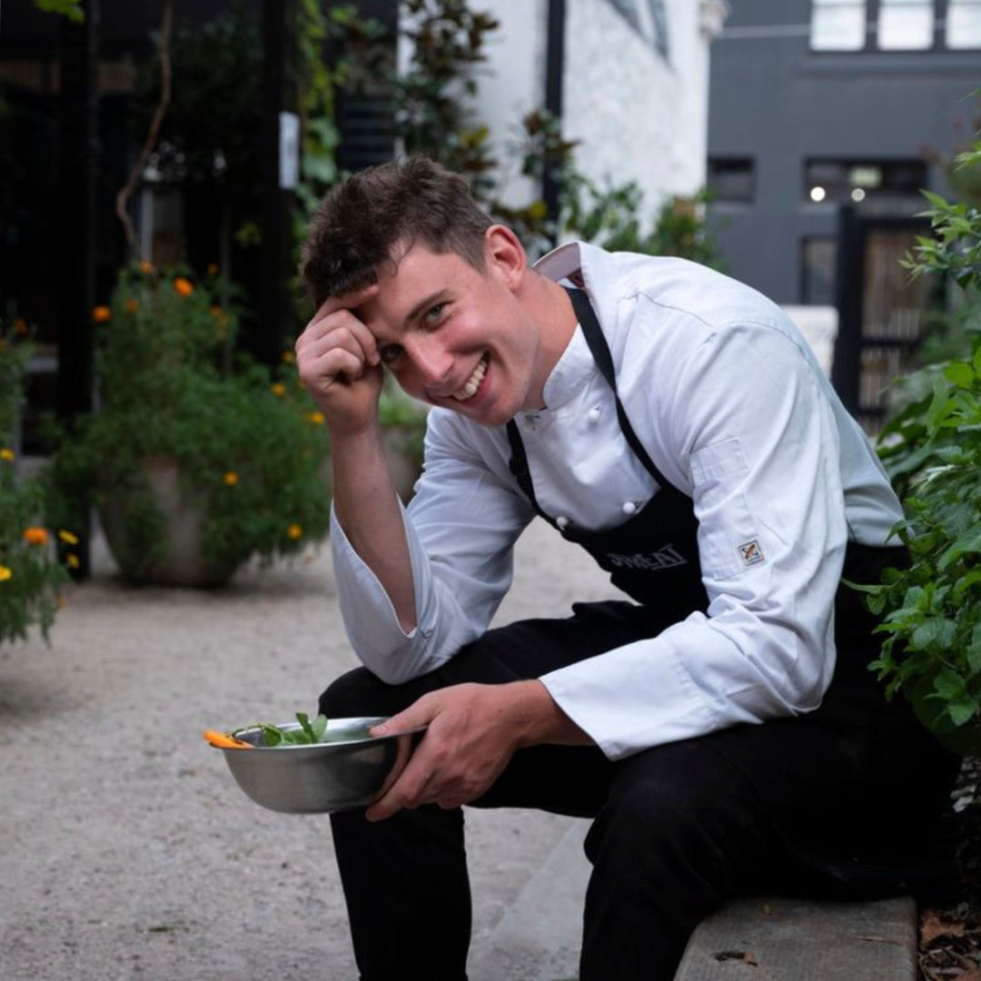 Chef from social enterprise STREAT preparing fresh food outdoors in Melbourne, highlighting hands-on hospitality training that supports young people facing barriers to employment.